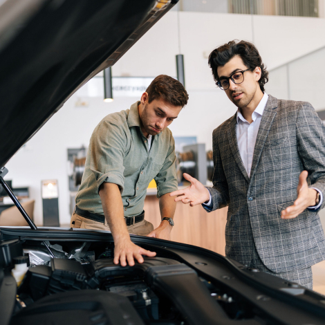 Portrait of professional dealer manager in business suit and male client near new car with open hood. Stylish friendly dealer talking about technical characteristics. Concept of choosing new auto
